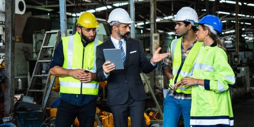 Industrial engineer and businessman in suite and safety helmet working in factory, planning, discussing and training workers with tablet in metalwork place , teamwork and team concept